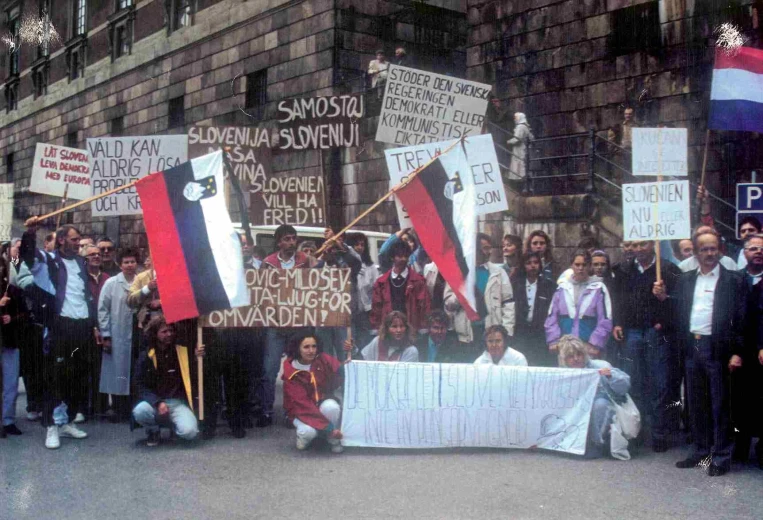 A huge crowd of smiling women in Slovenian national costumes at a demonstration are waving Slovenian flags and holding up banners with "Thank you Australia" written on them.