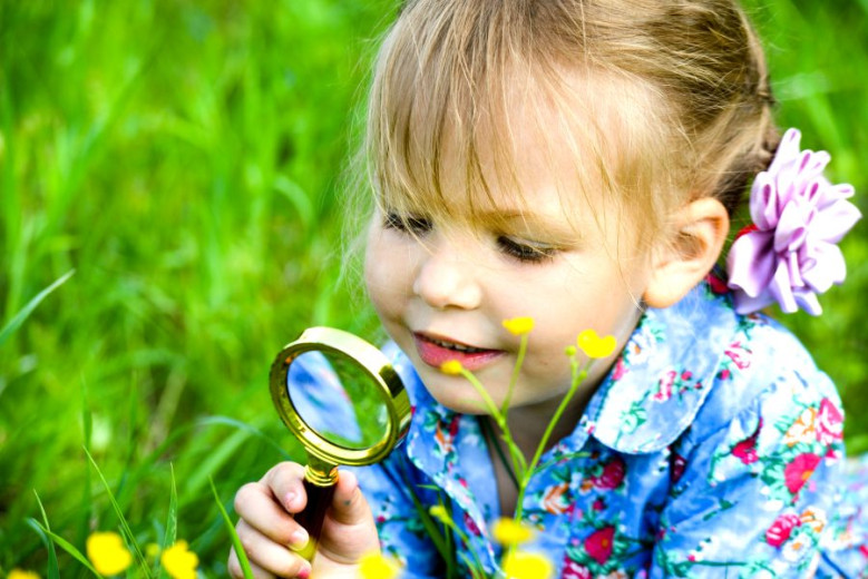 A girl explores a flower through a magnifying glass outdoors.