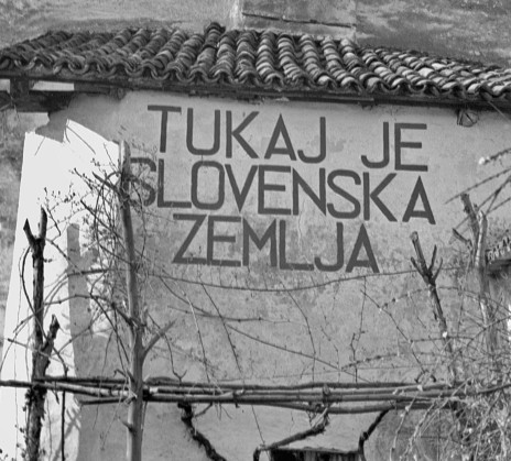 Black and white photo of a facade of a house. On it it's written "THIS IS SLOVENIAN LAND" in slovene.