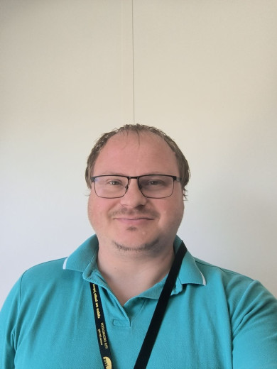 Bojan Vrtič wearing glasses and a teal polo shirt smiles at the camera.