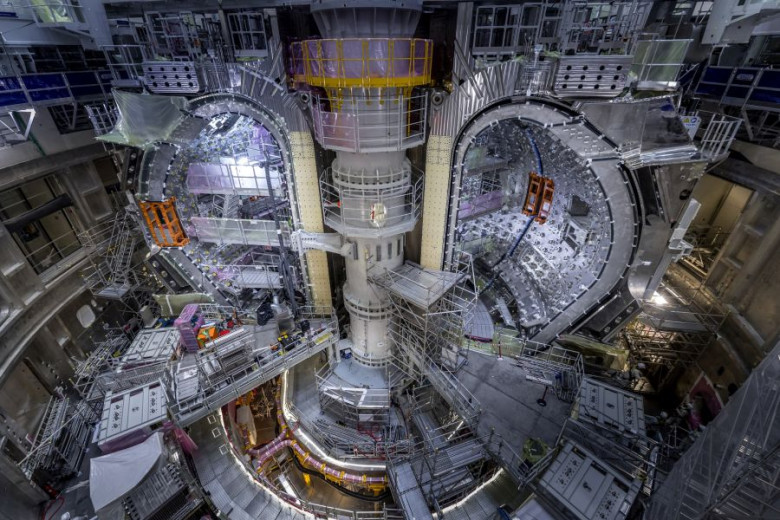 View of the ITER experimental fusion reactor assembly pit with installed vacuum vessel modules, surrounded by scaffolding and lifting equipment.