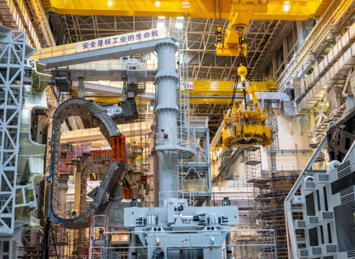 An industrial crane inside a manufacturing hall lifts one of the 18 D-shaped toroidal magnets, each 17 metres tall, that will generate the magnetic field needed to confine the plasma in the ITER reactor.