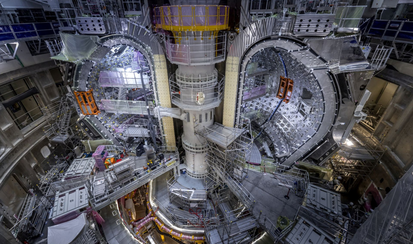 View of the ITER experimental fusion reactor assembly pit with installed vacuum vessel modules, surrounded by scaffolding and lifting equipment.