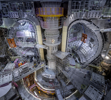 View of the ITER experimental fusion reactor assembly pit with installed vacuum vessel modules, surrounded by scaffolding and lifting equipment.