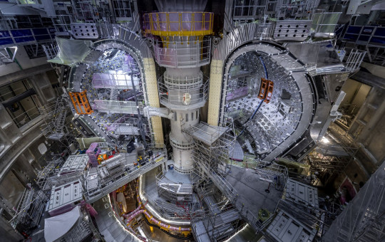 View of the ITER experimental fusion reactor assembly pit with installed vacuum vessel modules, surrounded by scaffolding and lifting equipment.