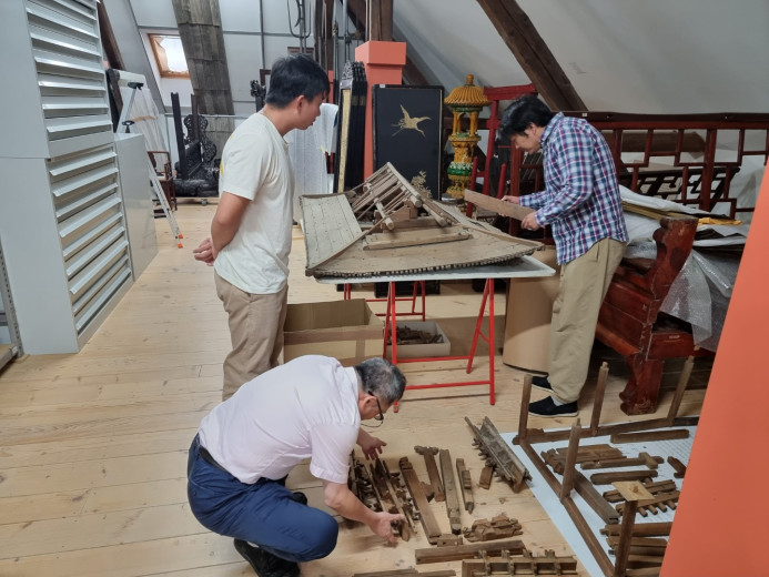 Three men are repairing a wooden model of a Chinese house.