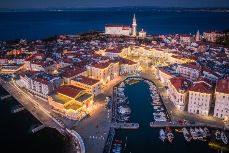 An aerial view of the town of Piran, with the town center decorated in yellow lights.