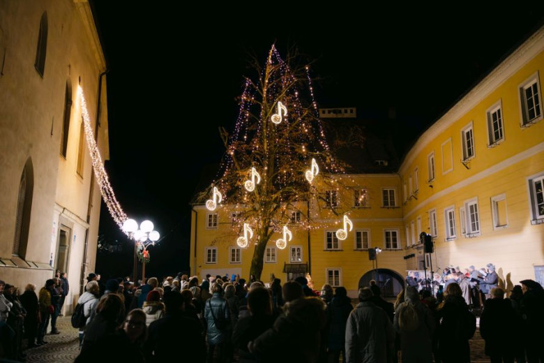 A crowd listening to a street concert beneath a tree decorated with glowing musical notes.