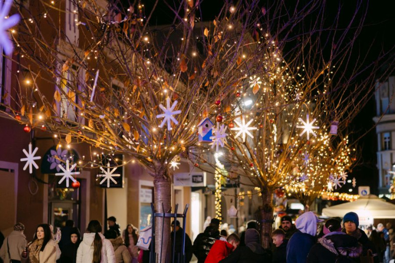 A street lined with trees decorated with festive yellow lights and snowflake-shaped ornaments.