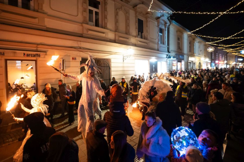 A crowd lines the streets of Celje, watching a parade of fairytale creatures carrying torches.