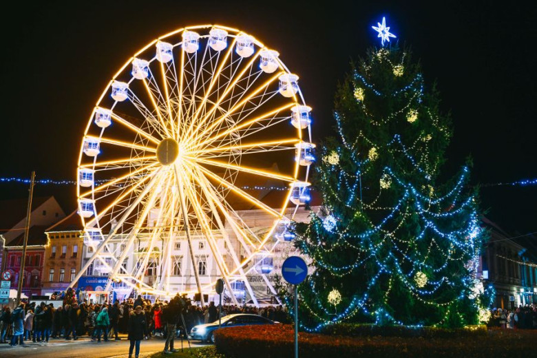 A giant Ferris wheel glowing in yellow light, next to a large Christmas tree adorned with blue and yellow ornaments and lights.