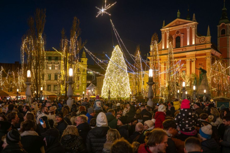 Prešeren Square in Ljubljana is packed with people admiring the holiday lights. In the center of the square stands an illuminated Christmas tree.