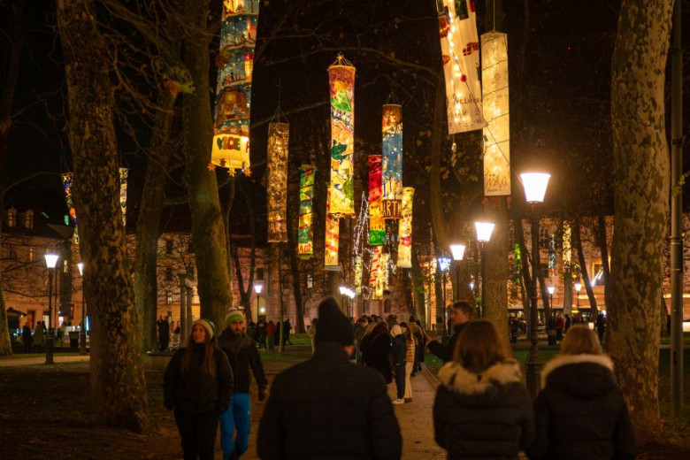 People stroll beneath the trees in the park, adorned with festive lanterns.