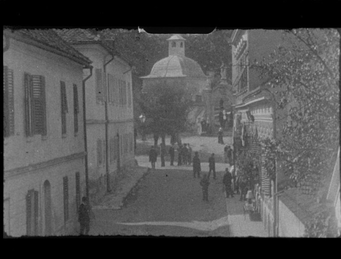 A black and white photo depicting a street with a few people and a church in the background.