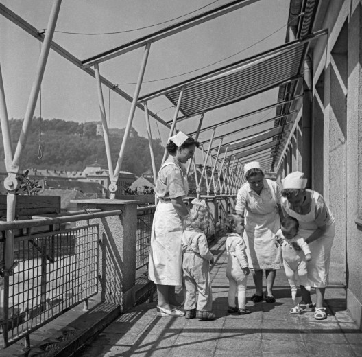 Črno-bela fotografija treh medicinskih sester in treh majhnih otrok na balkonu Pediatrične klinike v Ljubljani.