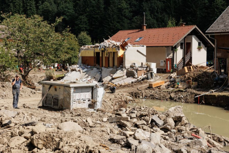 This photo shows a hous that was partially swept away by the floods. HAlf of the house is missing. On the right of the picture you can still see a big muddy puddle and debris brought by the water – furniture, branches.