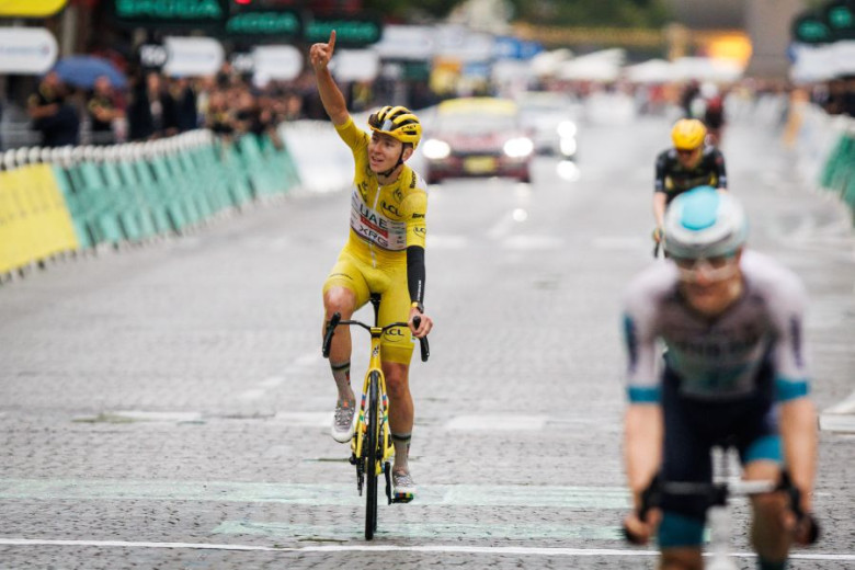 A photo of cyclist Tadej Pogačar triumphantly crossing the Tour de France finish line, his right arm raised high in celebration.