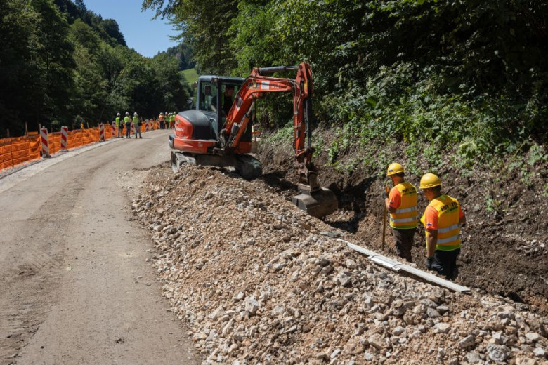 The image shows a partially reconstructed dirt road. The repairs are still taking place two workers and an excavator are present on the side of the road.