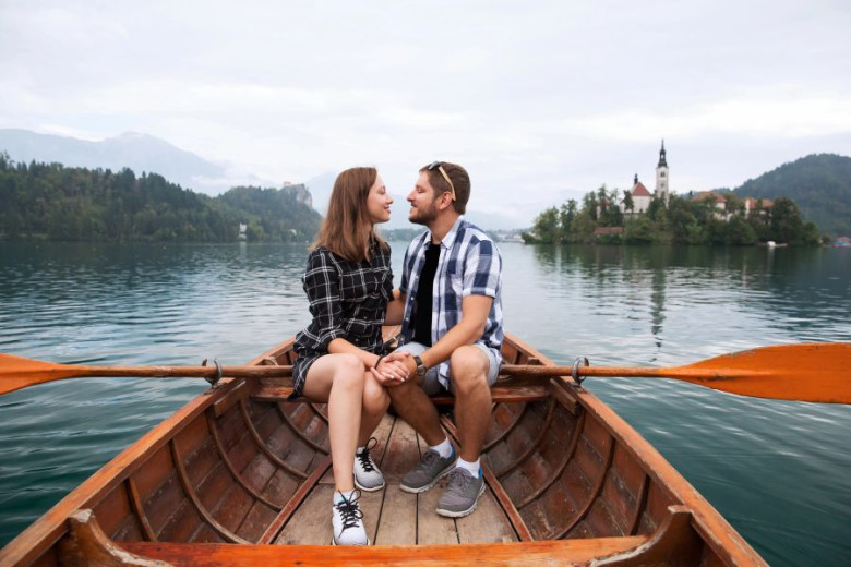 Young couple in a boat on a lake. In the backround there is a small island with a church on it.