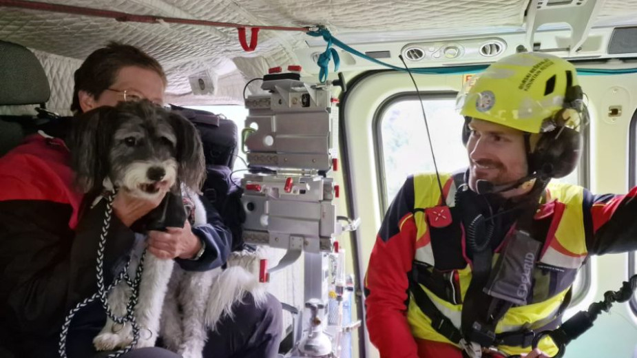 This photo shows the interior of a rescue helicopter, where two members of the Mountain Rescue Service are looking at a dog sitting in the lap of one of them.