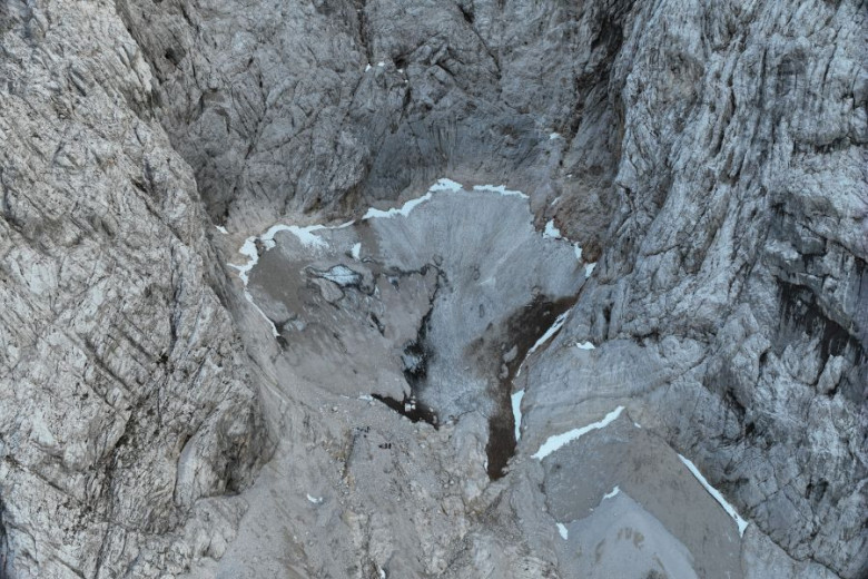 The photo shows grey rocky terrain in the Kamnik-Savinja Alps with a patch of ice and snow in the middle. 