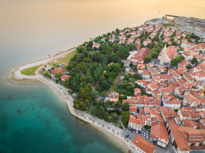 Fotografija majhnega obmorskega mesteca in njegove plaže v večerni svetlobi.