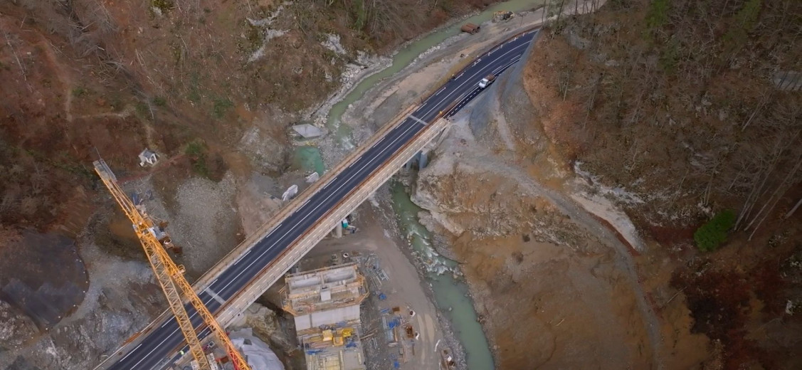 This is an aerial photo of a newly constructed bridge, featuring fresh asphalt and a small river flowing beneath it.