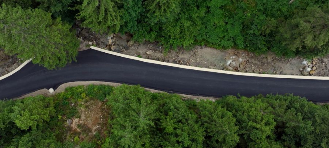 This is an aerial photo showing an asphalt road winding through a forested landscape.