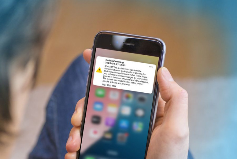 Close-up of a hand holding a smartphone displaying a national warning test message from the Republic of Slovenia's Civil Protection and Disaster Relief administration.