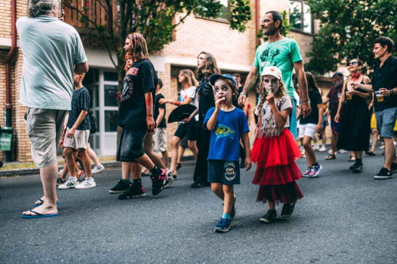 This photo shows a group of people walking down the street. In the foreground, two children are dressed as zombies, their faces painted with eerie makeup.