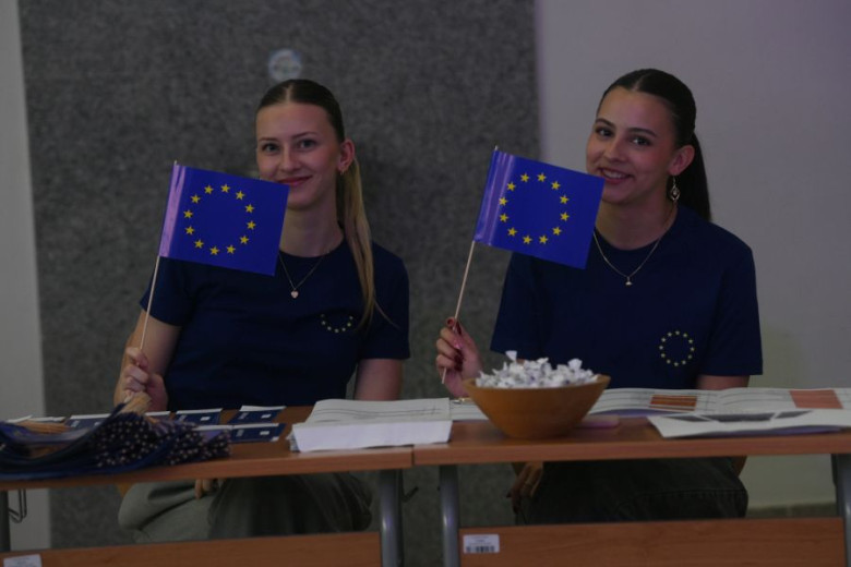 Two young girls holding flags featuring a circle of twelve golden stars on a blue background.