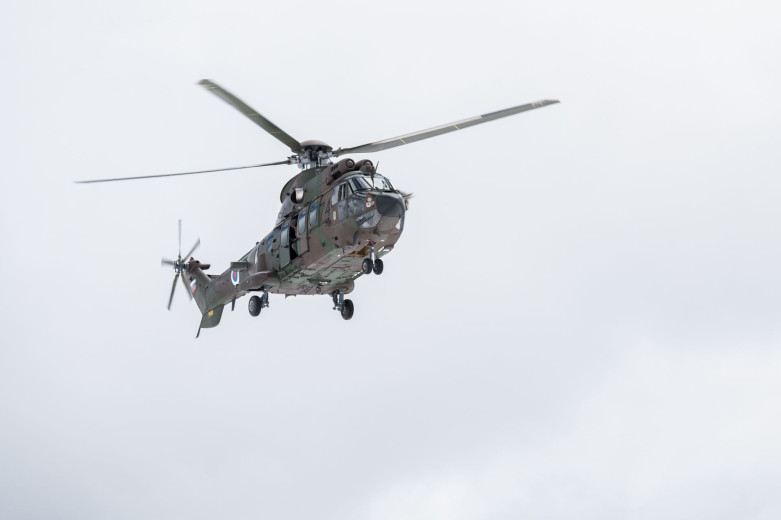 Fotografija vojaškega helikopterja v maskirnih barvah (v različnih odtenkih zelene) med letom.