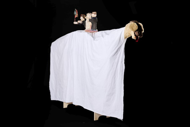 A white cloth covers a simple structure with small figures on top and an animal head on one side.