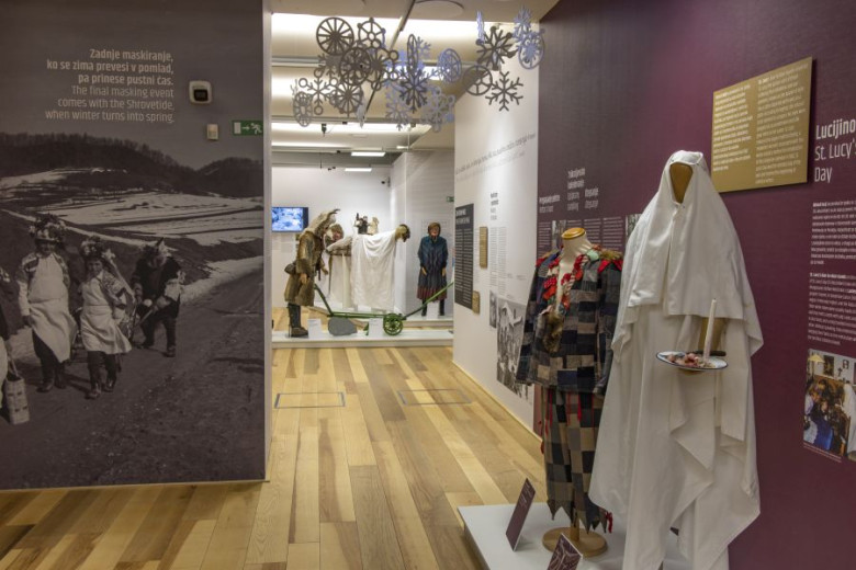 An exhibition room with mannequins in carnival costumes, wall texts, photos, and wooden flooring.