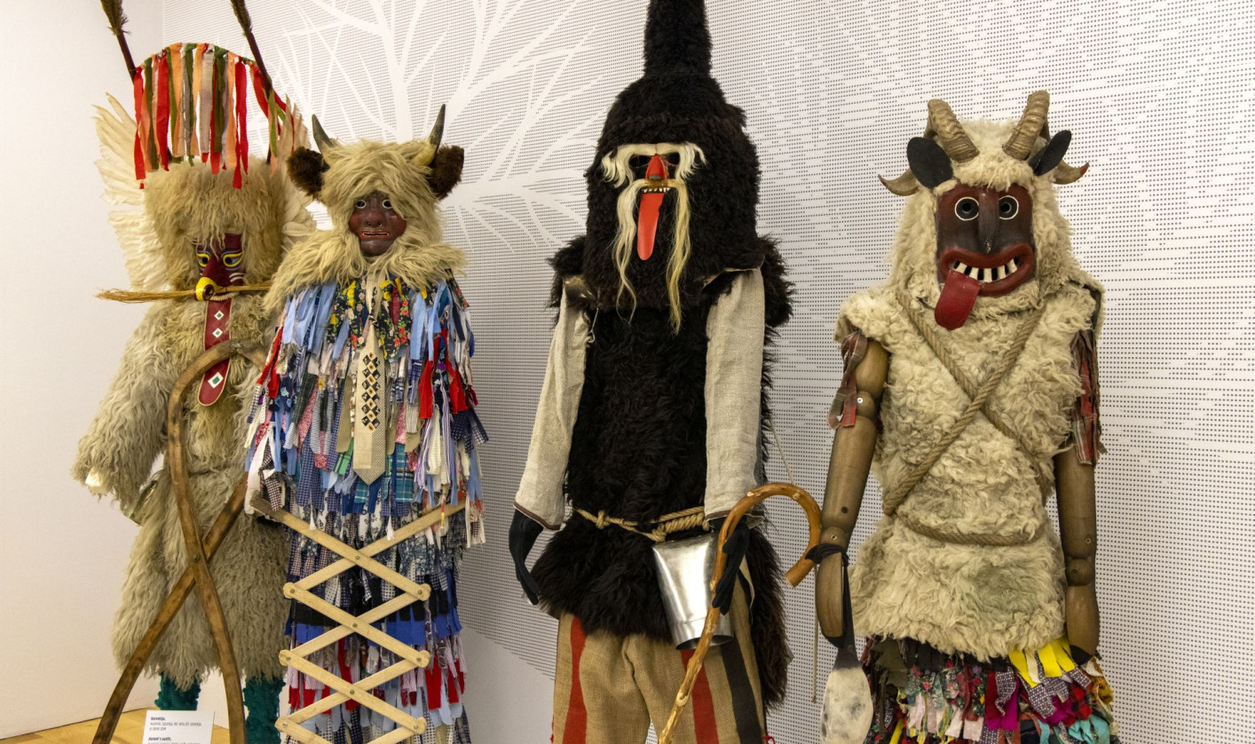 Štiri pustne oprave z rogastimi maskami, krznom, zvonci in pisanimi trakovi stojijo druga ob drugi.