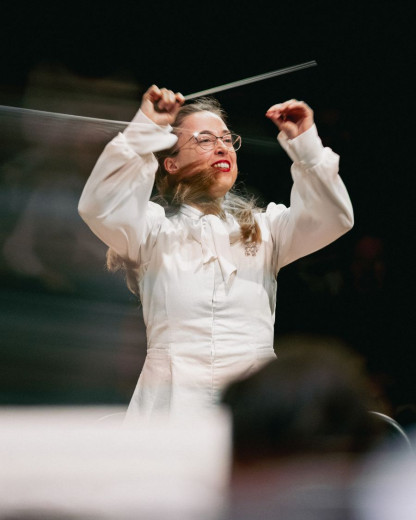 Mojca Lavrenčič passionately directs an orchestra with her hands in the air.