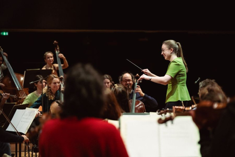 Mojca Lavrenčič conducting at the La Maestra competition. The conductor stands in the center, surrounded by the musicians.