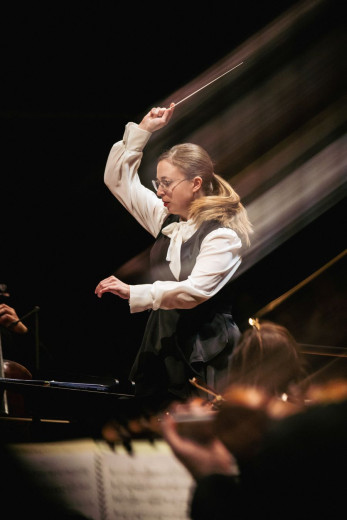 Conductor Mojca Lavrenčič energetically leads an orchestra, her baton a blur of motion. 