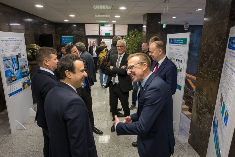 A group of people are gathered in a hallway near research posters, engaged in conversation. 