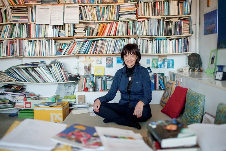 Manca Košir sitting in a room surrounded by bookshelves filled with books.