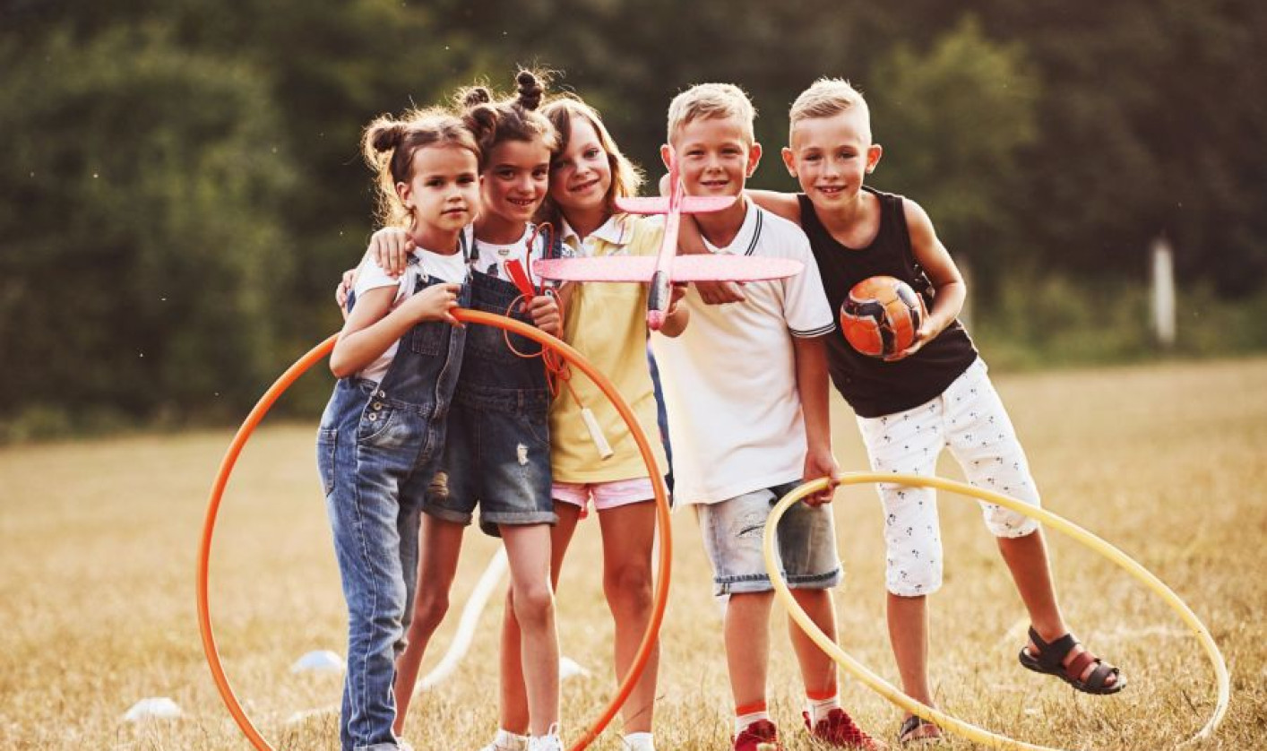 A group of children plays on a field with hoops and a ball. They stand close together, smiling.