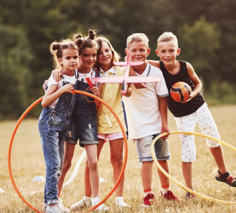 A group of children plays on a field with hoops and a ball. They stand close together, smiling.