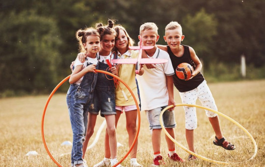 A group of children plays on a field with hoops and a ball. They stand close together, smiling.