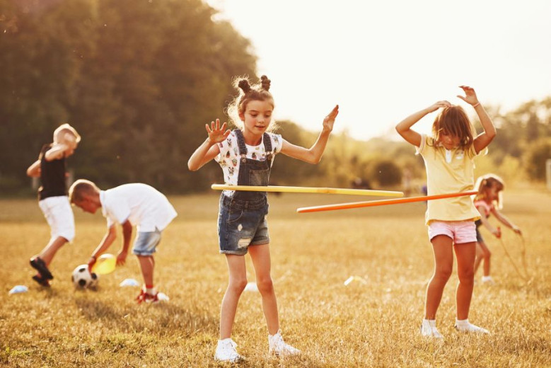 Children play with hula hoops and a ball on a sunny field.