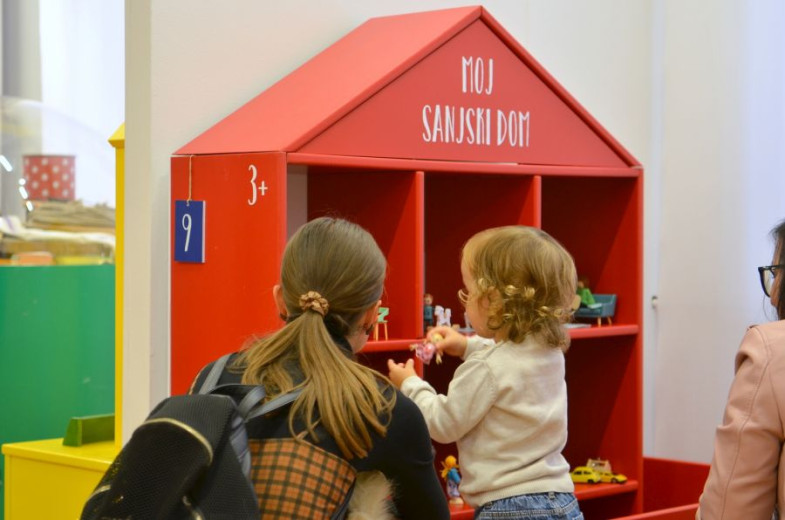 A child and a woman in the front of the toy house