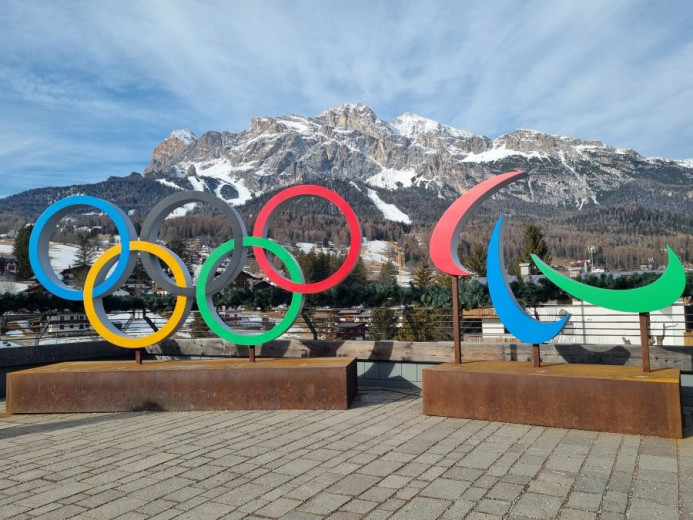 Olimpijski in paraolimpijski simboli postavljeni na trgu, v ozadju pa so zasnežene gore. 