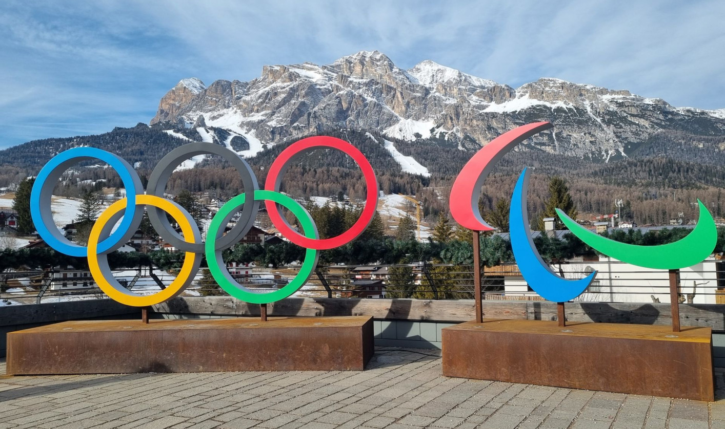 Sculptures of Olympic and Paralympic symbols on a plaza, with a snow-capped mountain under a blue sky in the background.
