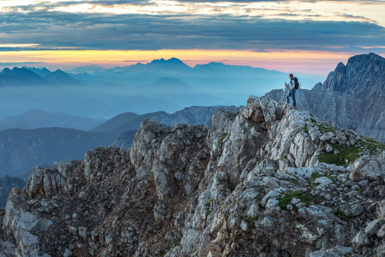 A woman is standing on the top of the mountain and has a beautiful view in the evening light.