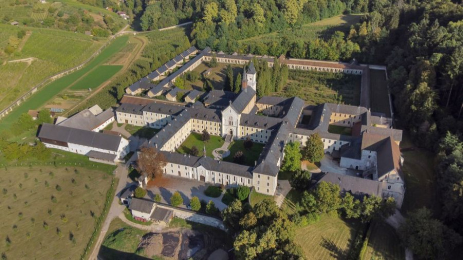 Pogled z zraka na velik, zgodovinski samostanski kompleks, obdan z bujnim zelenjem in polji, z osrednjim dvoriščem in spokojnim, mirnim vzdušjem.