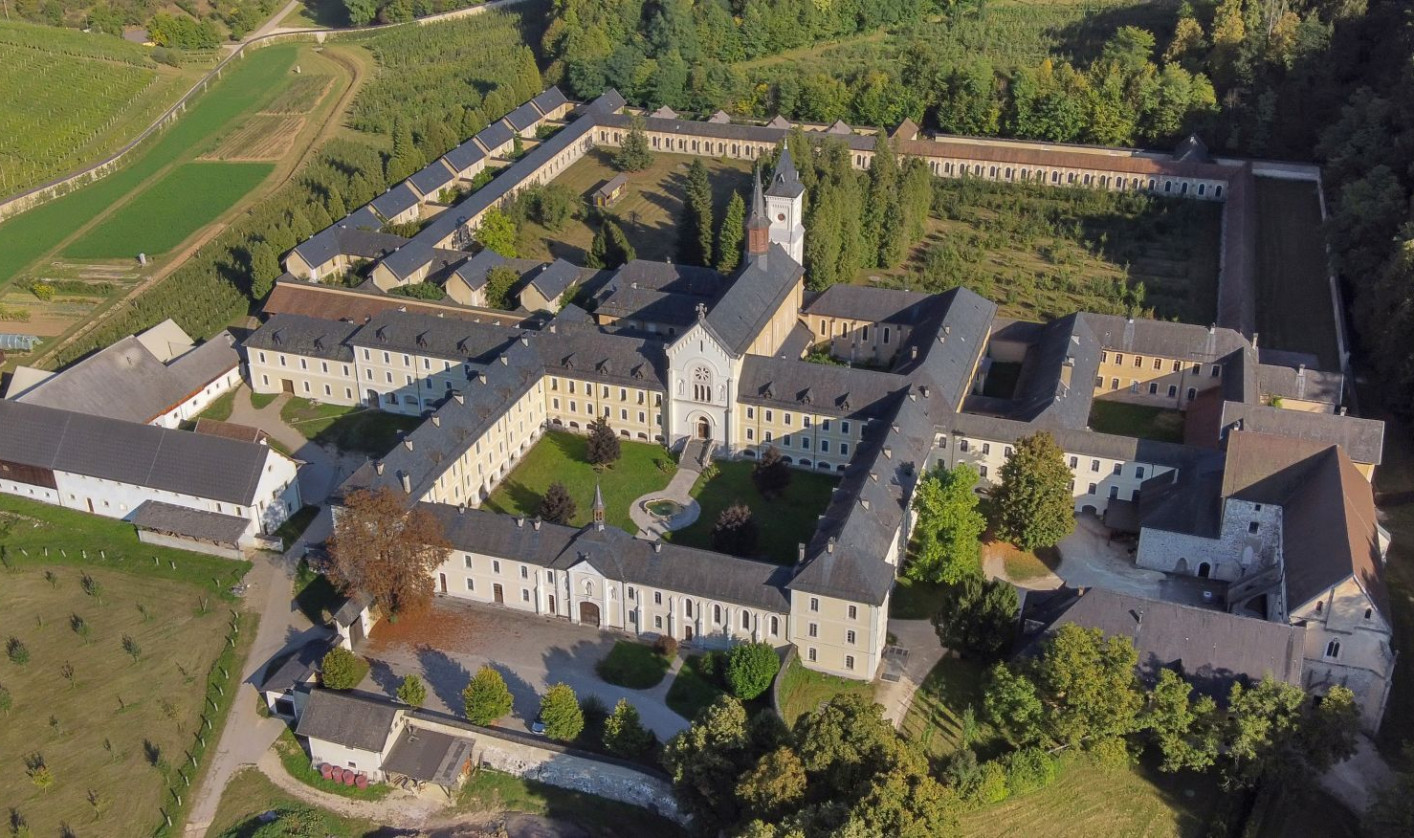 Aerial view of a large, historic monastery complex surrounded by lush greenery and fields, with a central courtyard and a serene, peaceful ambiance.